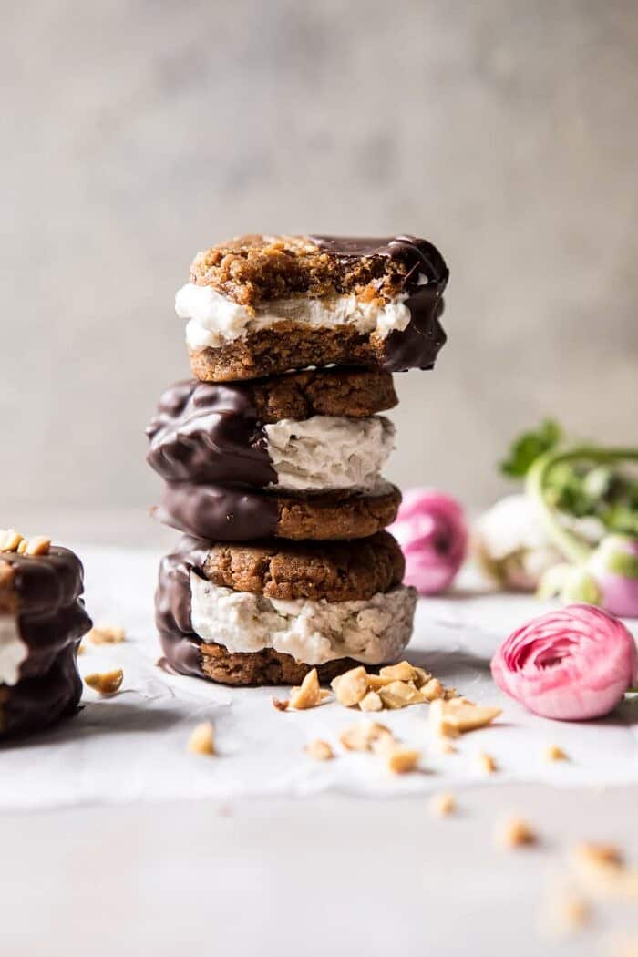 Chocolate Dipped Peanut Cookie Ice Cream Sandwiches | halfbakedharvest.com #icecream #chocolate #peanutbutter #summer stacked front on photo of Chocolate Dipped Peanut Cookie Ice Cream Sandwiches with bite out of sandwich