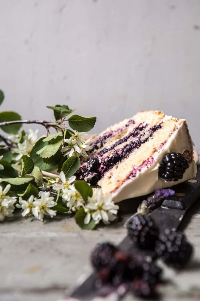 Blackberry Lavender Naked Cake with White Chocolate Buttercream | halfbakedharvest.com #summerrecipes #layercake #blueberries side angled photo of Blackberry Lavender Naked Cake with White Chocolate Buttercream with one slice