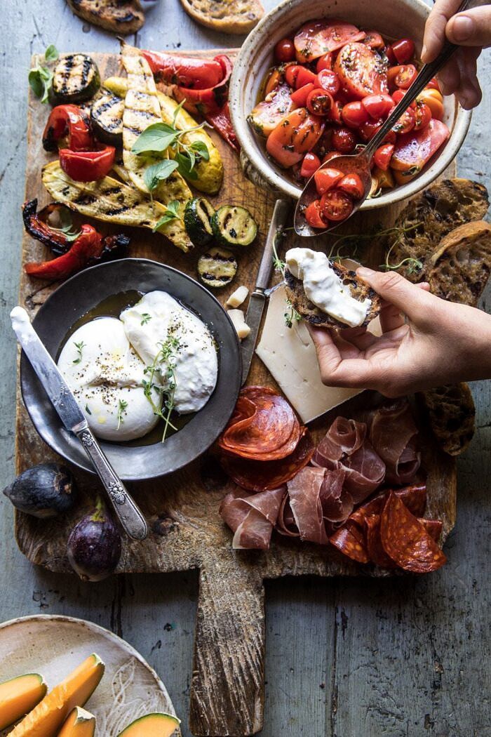 Marinated Tomato and Grilled Veggie Cheese Board | halfbakedharvest.com #cheeseboard #summerrecipes #easy #4thofjulyrecipe overhead photo of Marinated Tomato and Grilled Veggie Cheese Board with hands in photo