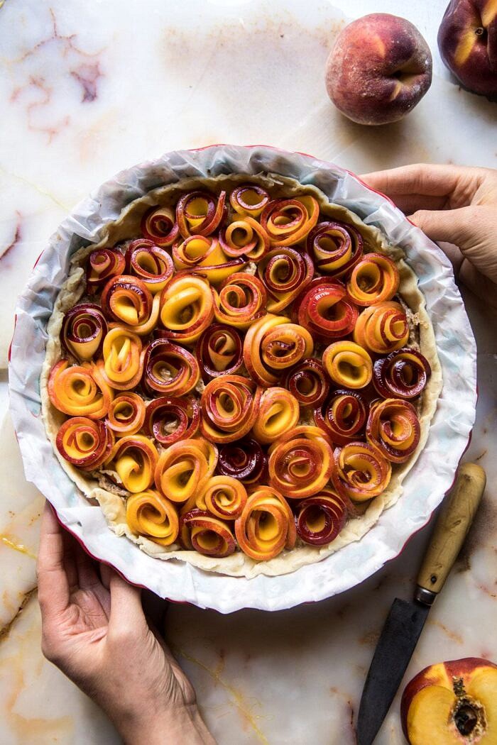 Sweet Peach Rose Tart | halfbakedharvest.com #peach #summerrecipes #tart #summer #pie overhead photo of raw Sweet Peach Rose Tart with hands in photo before baking