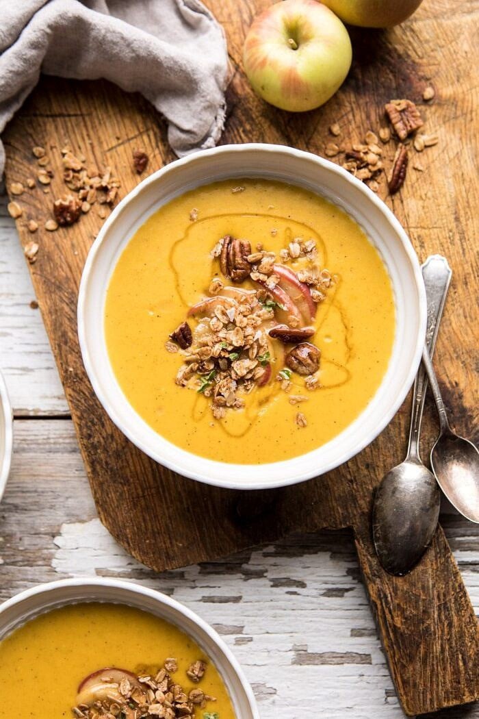 Cheddar Apple Butternut Squash Soup with Cinnamon Pecan Crumble | halfbakedharvest.com #soup #butternutsquash #autumnrecipes #thanksgiving overhead photo of Cheddar Apple Butternut Squash Soup with Cinnamon Pecan Crumble with apples and spoon in photo