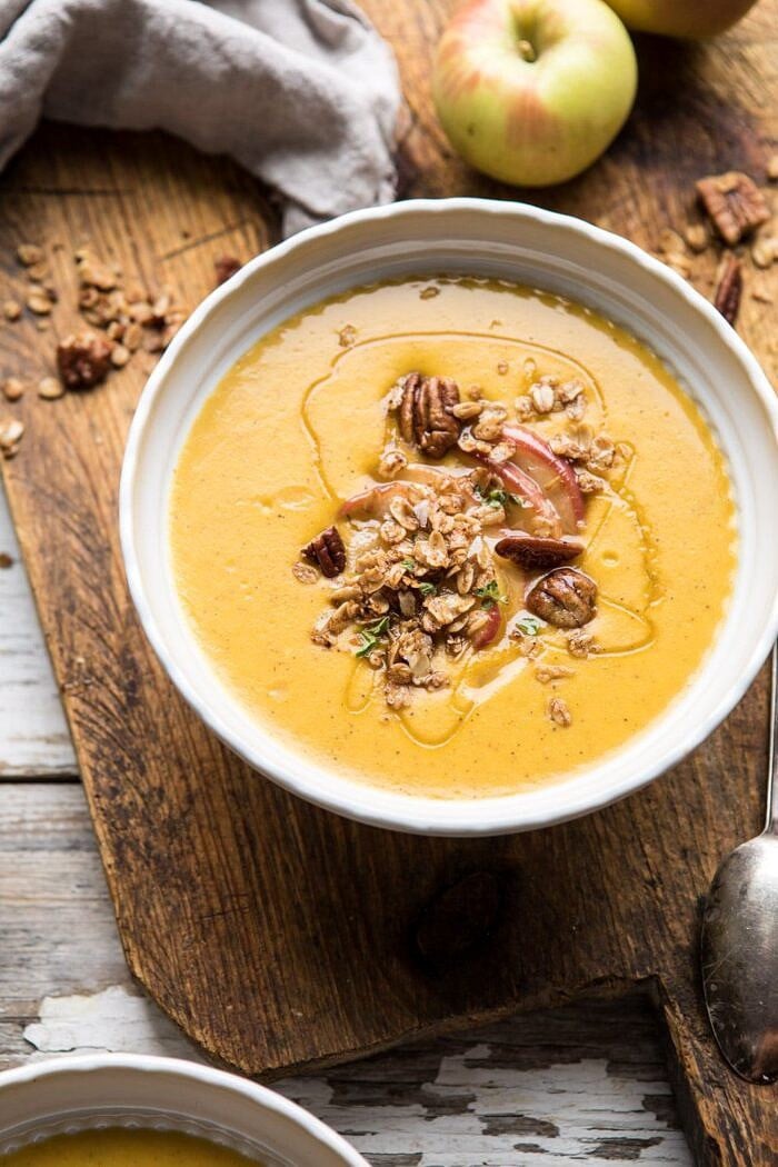 Cheddar Apple Butternut Squash Soup with Cinnamon Pecan Crumble | halfbakedharvest.com #soup #butternutsquash #autumnrecipes #thanksgiving close up, side angle photo of Cheddar Apple Butternut Squash Soup with Cinnamon Pecan Crumble with apples in photo