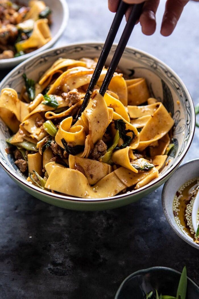 Better Than Takeout Szechuan Noodles with Sesame Chili Oil | halfbakedharvest.com #dinner #noodles #easyrecipes #chinese side angled photo of Better Than Takeout Szechuan Noodles with Sesame Chili Oil with chopsticks in bowl
