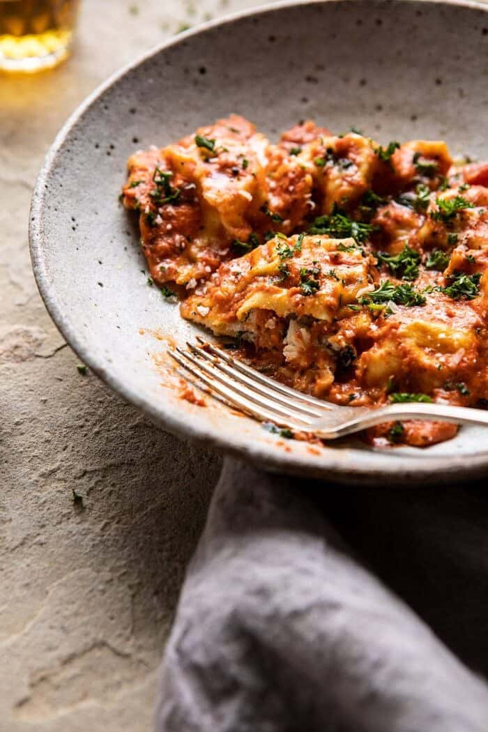 side angle close up photo of Brown Butter Lobster Ravioli with Tomato Cream Sauce with bite take out of ravioli