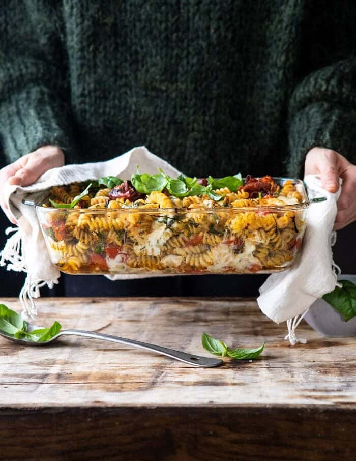 Caprese Pesto Pasta Bake | halfbakedharvest.com #caprese #pesto #pasta #easyrecipes front on photo of Caprese Pesto Pasta Bake with person holding baking dish