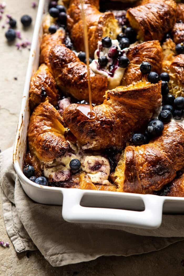 Berry and Cream Cheese Croissant French Toast Bake | halfbakedharvest.com #frenchtoast #brunch #easyrecipes #springrecipes #easter side angled photo of Berry and Cream Cheese Croissant French Toast Bake with maple being drizzled on top