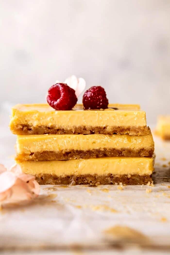 Creamy Lemon Bars with Browned Butter Raspberries | halfbakedharvest.com #lemon #brownbutter #spring #summer #easter #mothersday #brunch #dessert side angled photo of Creamy Lemon Bars stacked on top of each other