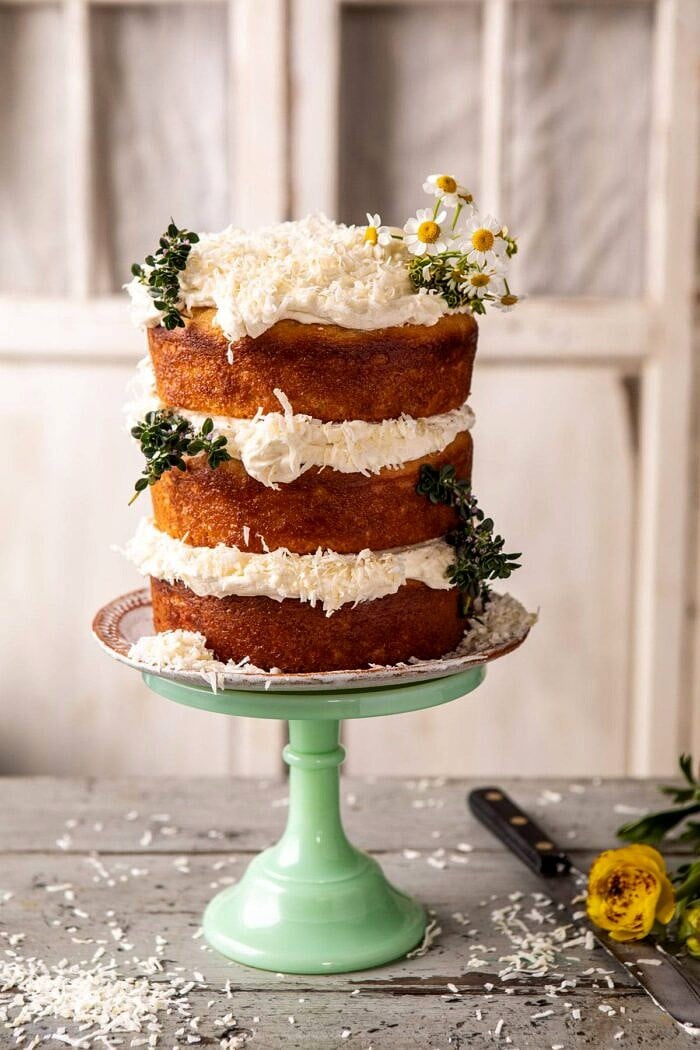 Lemon Coconut Naked Cake with Whipped Vanilla Buttercream | halfbakedharvest.com #coconutcake #springrecipes #easter #cake #layercake side angled photo of Lemon Coconut Naked Cake with Whipped Vanilla Buttercream on cake stand