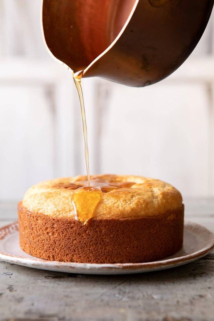 Lemon Coconut Naked Cake with Whipped Vanilla Buttercream | halfbakedharvest.com #coconutcake #springrecipes #easter #cake #layercake lemon honey syrup being drizzled on Lemon Coconut Naked Cake