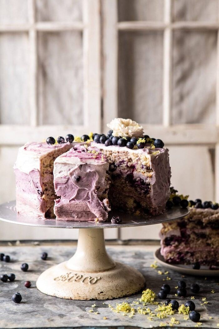 Bursting Blueberry Lemon Layer Cake | halfbakedharvest.com #bleberrycake #layercake #summerrecipes #dessert side angled photo of Bursting Blueberry Lemon Layer Cake with slices cut out