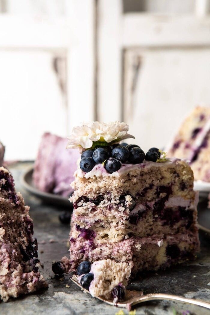 Bursting Blueberry Lemon Layer Cake | halfbakedharvest.com #bleberrycake #layercake #summerrecipes #dessert side angled photo of Bursting Blueberry Lemon Layer Cake slices with bite taken out
