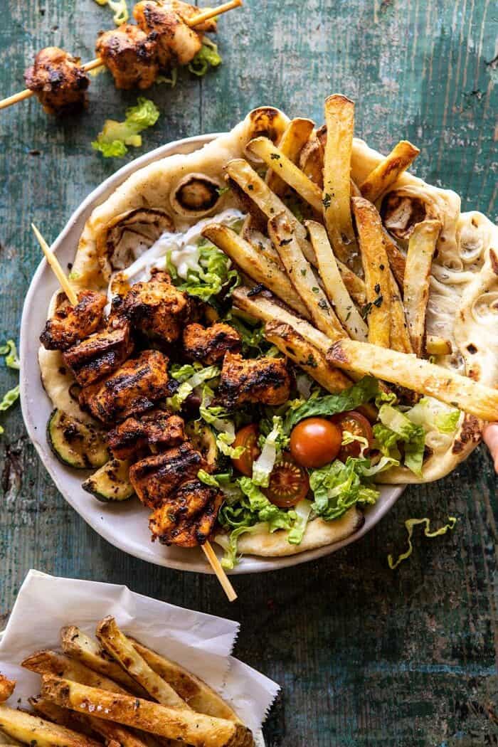Chicken Souvlaki Bowls with Garlic Fries | halfbakedharvest.com #greek #healthyrecipes #dinner #summerrecipes overhead photo of Chicken Souvlaki Bowls with Garlic Fries and chicken off of stick in bowl