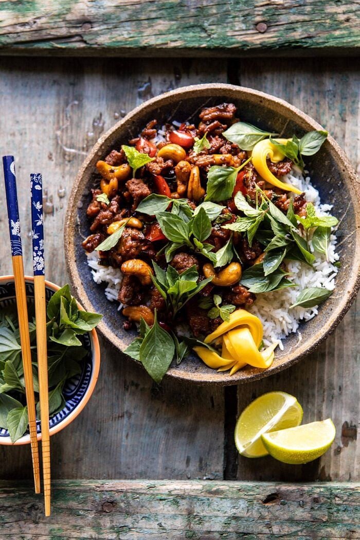 Better Than Takeout Sweet Thai Basil Chicken | halfbakedharvest.com #easyrecipes #20minutes #thaichicken #ricebowl #healthy overhead photo of Better Than Takeout Sweet Thai Basil Chicken with chopsticks resting on bowl and limes on table
