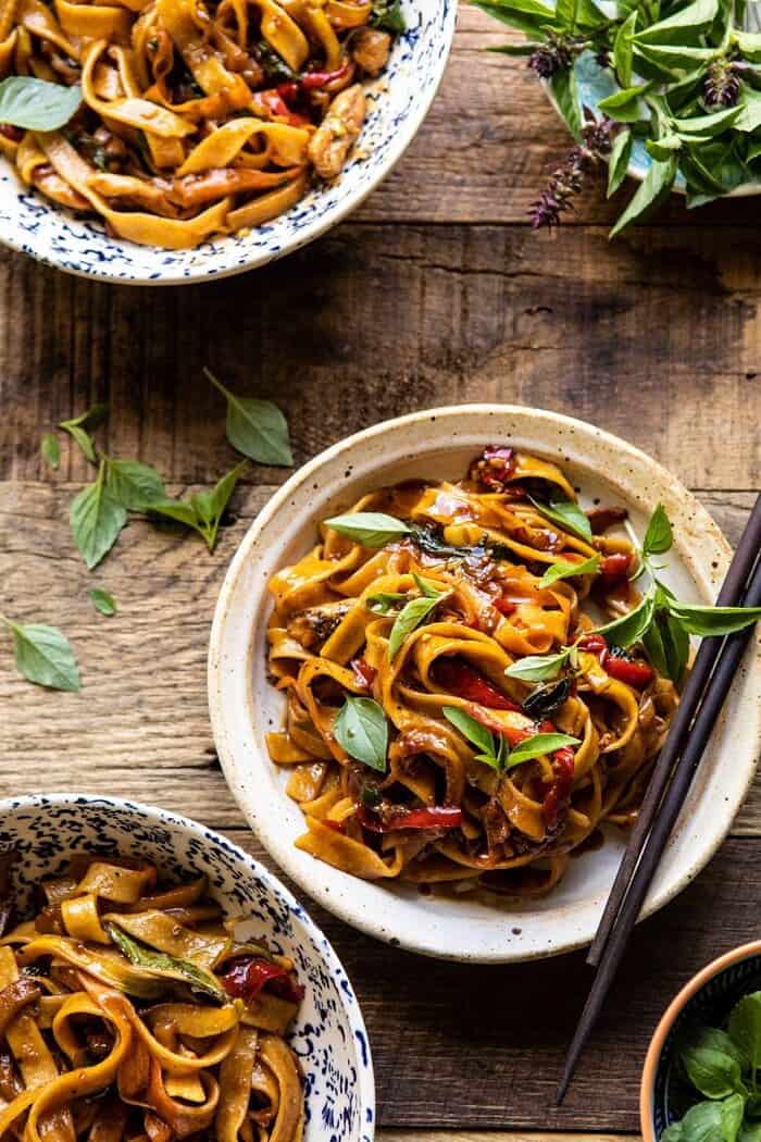 Better Than Takeout Thai Drunken Noodles | halfbakedharvest.com #takeout #noodles #weeknightrecipe #Thai overhead photo of Better Than Takeout Thai Drunken Noodles with chopstick resting on bowl and basil on wood surface
