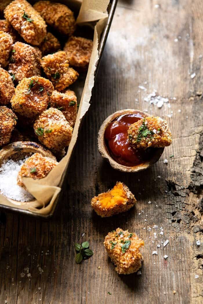 Baked Sweet Potato Parmesan Tater Tots | halfbakedharvest.com #sweetpotatoes #healthy #easyrecipes #gameday #tatertots side angled photo of Baked Sweet Potato Parmesan Tater Tot sitting in ketchup