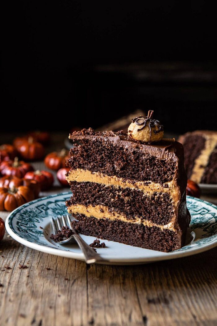 Pumpkin Patch Chocolate Peanut Butter Cake | halfbakedharvest.com #chocolatepeanutbutter #chocolatecake #peanutbutter #halloween side angle photo of Pumpkin Patch Chocolate Peanut Butter Cake slice on plate with mimi pumpkins in the background