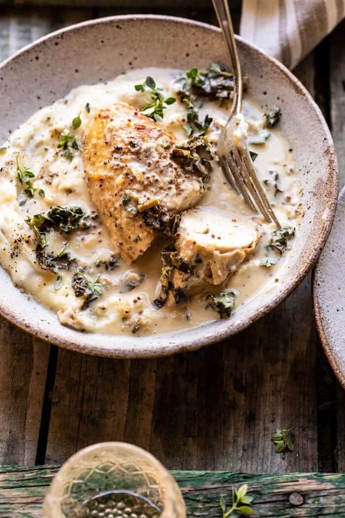 Slow Cooker French Wine and Mustard Chicken | halfbakedharvest.com #slowcooker #crockpot #instantpot #chicken side angled photo of Slow Cooker French Wine and Mustard Chicken with chicken cut in half and sitting in mustard sauce