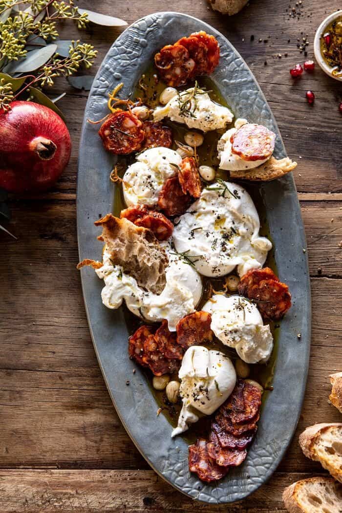 Burrata with Lemon Pepper Salami Bites | halfbakedharvest.com #burrata #appetizer #christmas overhead photo of Burrata with Lemon Pepper Salami Bites on serving plate with pomegranate on table