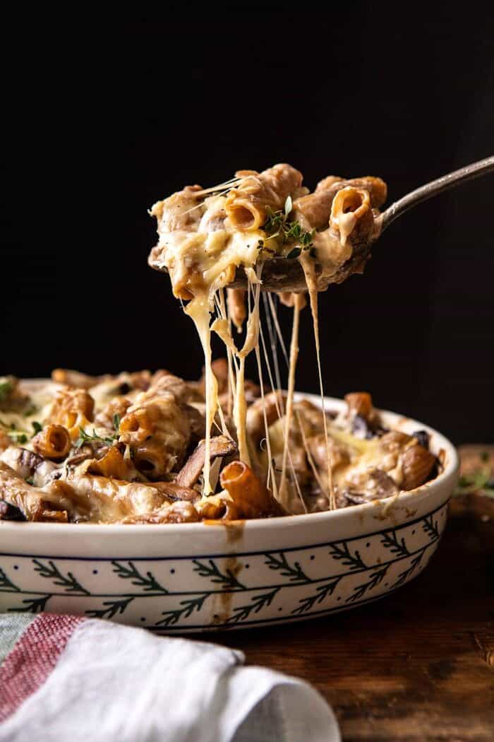 One Pot Creamy French Onion Pasta Bake | halfbakedharvest.com #pasta #frenchonion #easyrecipes side angled photo of One Pot Creamy French Onion Pasta Bake with serving spoon pulling pasta out of the baking dish