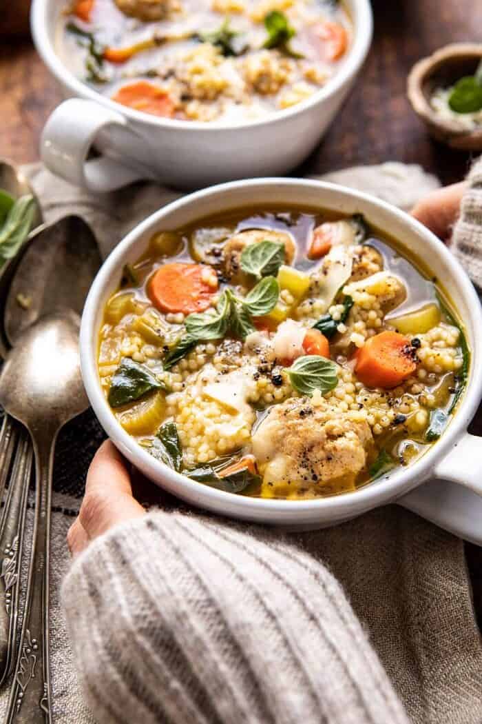 side angled close up photo of Healthier Italian Wedding Soup with Lemon and Garlic and hands on soup bowl