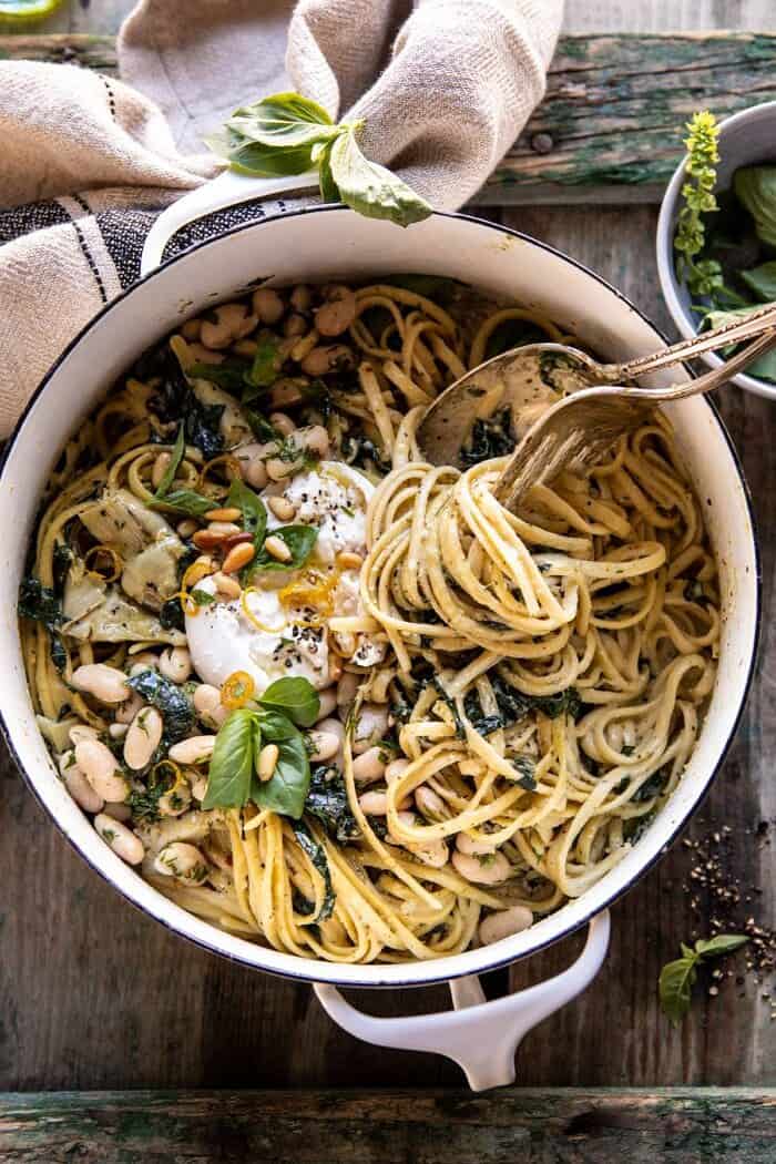 One Pot Creamy Tuscan Pesto and Artichoke Pasta | halfbakedharvest.com #onepot #pasta overhead photo of One Pot Creamy Tuscan Pesto and Artichoke Pasta with fork in pasta twirling the pasta up