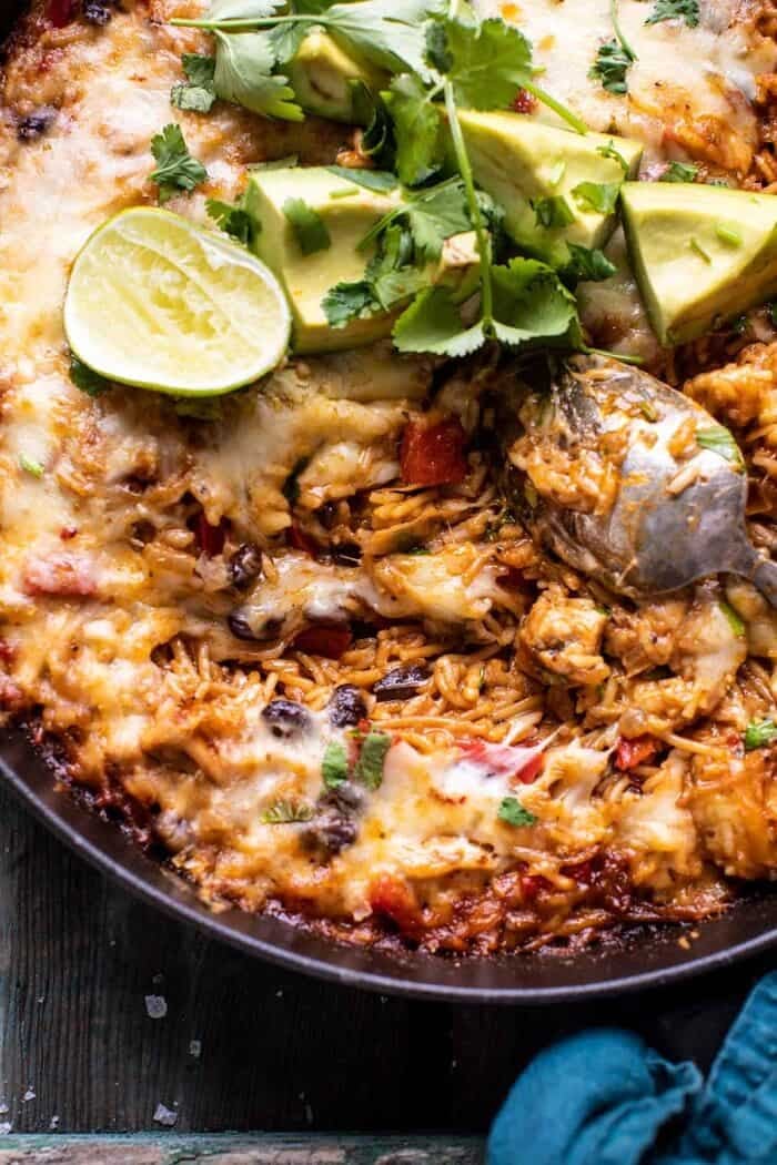 One Skillet Cheesy Cuban Chicken Rice Bake | halfbakedharvest.com overhead close up photo of One Skillet Cheesy Cuban Chicken Rice Bake with cheese melted and spoon in skillet pulling up the cheese