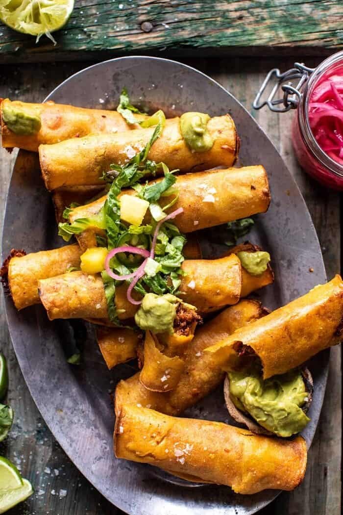 Crispy Chicken Tinga Taquitos with Salty Lime Avocado Crema | halfbakedharvest.com overhead photo of Crispy Chicken Tinga Taquitos with 1 taquito broken in half