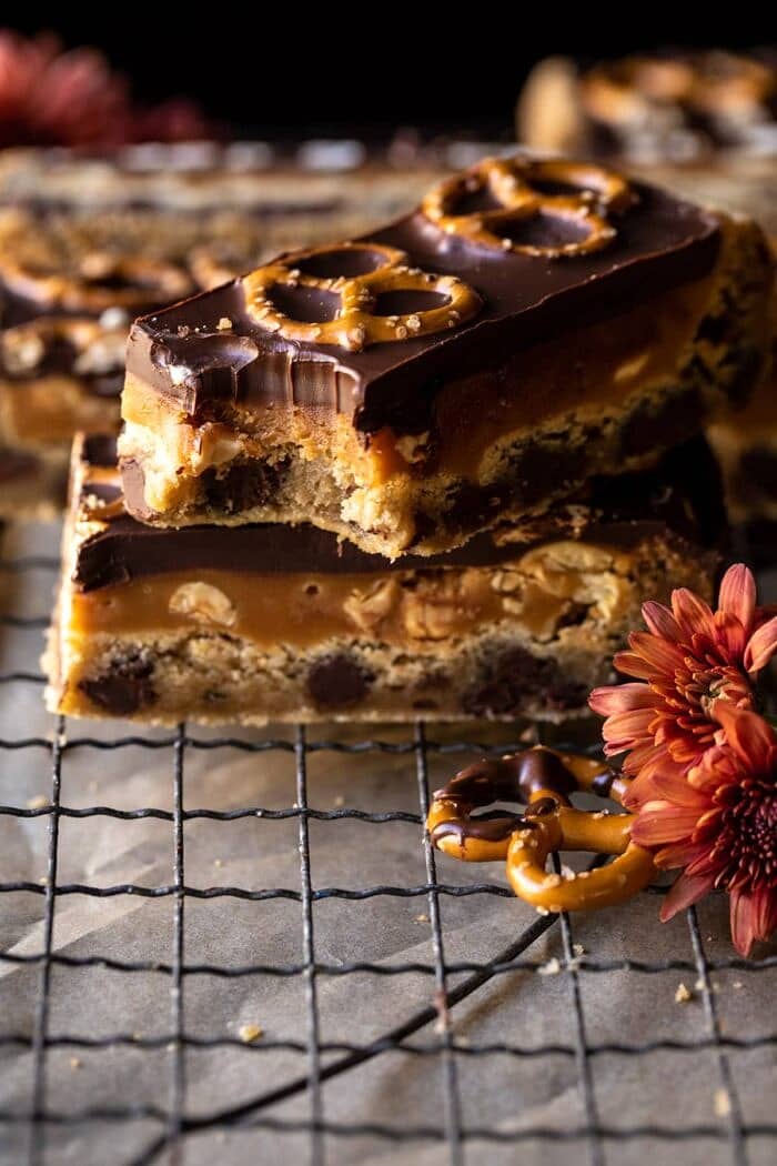 Salted Pretzel Chocolate Chip Cookie Snickers Bars | halfbakehavrest.com side angled photo of Salted Pretzel Chocolate Chip Cookie Snickers Bars with bite taken out of bar
